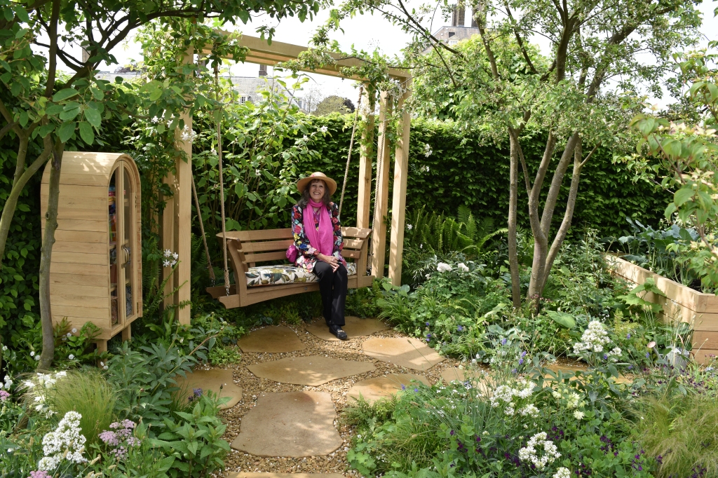 Jenny Rose Carey on a bench next to a little library at the Chelsea Flower Show 2023